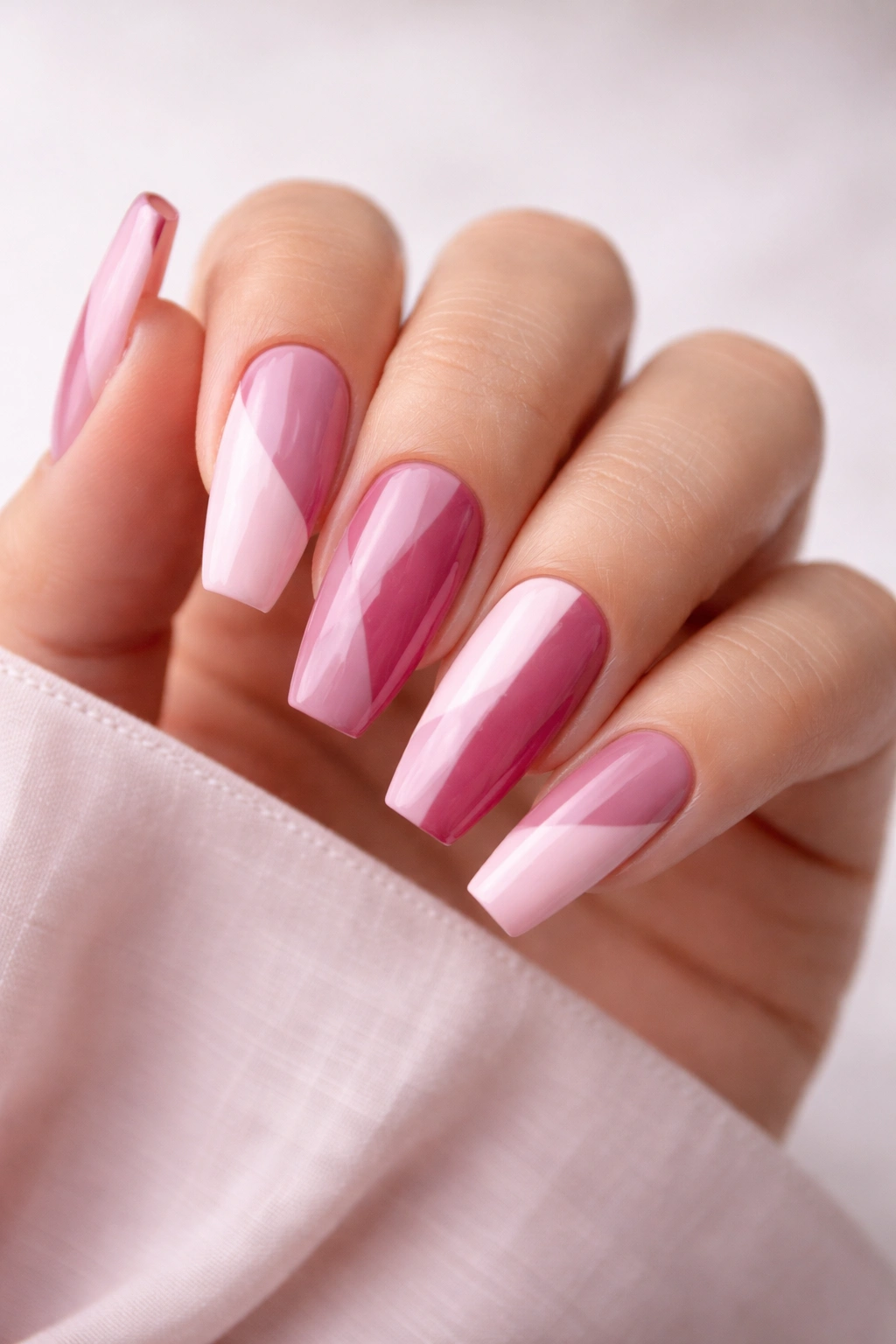 Close-up of ballerina nails with two-tone pink color-blocks in milky pink and dusty rose against a neutral backdrop