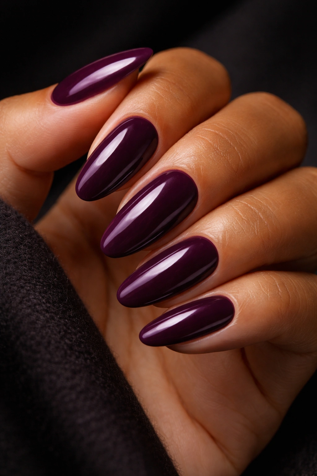 Close-up of moody plum nails on medium skin with deep purple-red tone