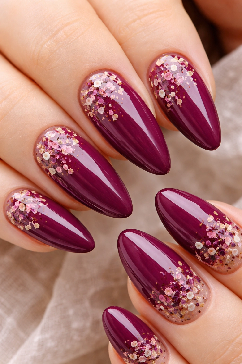Close-up of almond nails in deep mulberry with dried flower petals embedded in clear gel