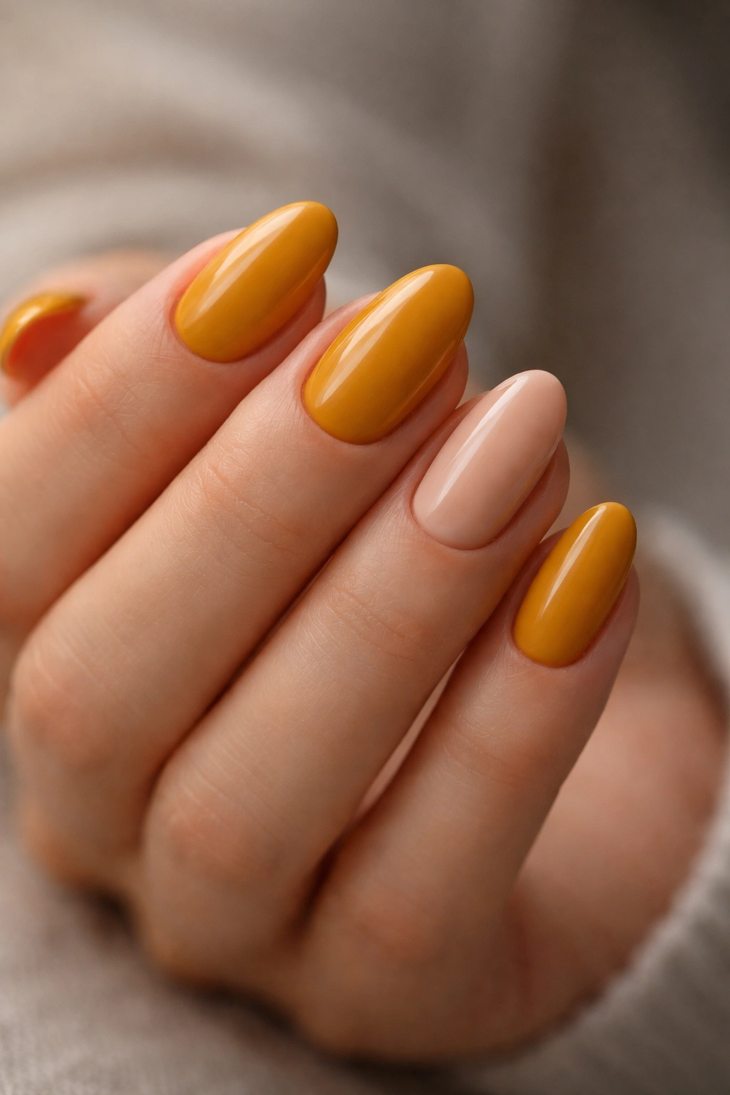 Close-up of short almond nails with mustard yellow and single nude accent