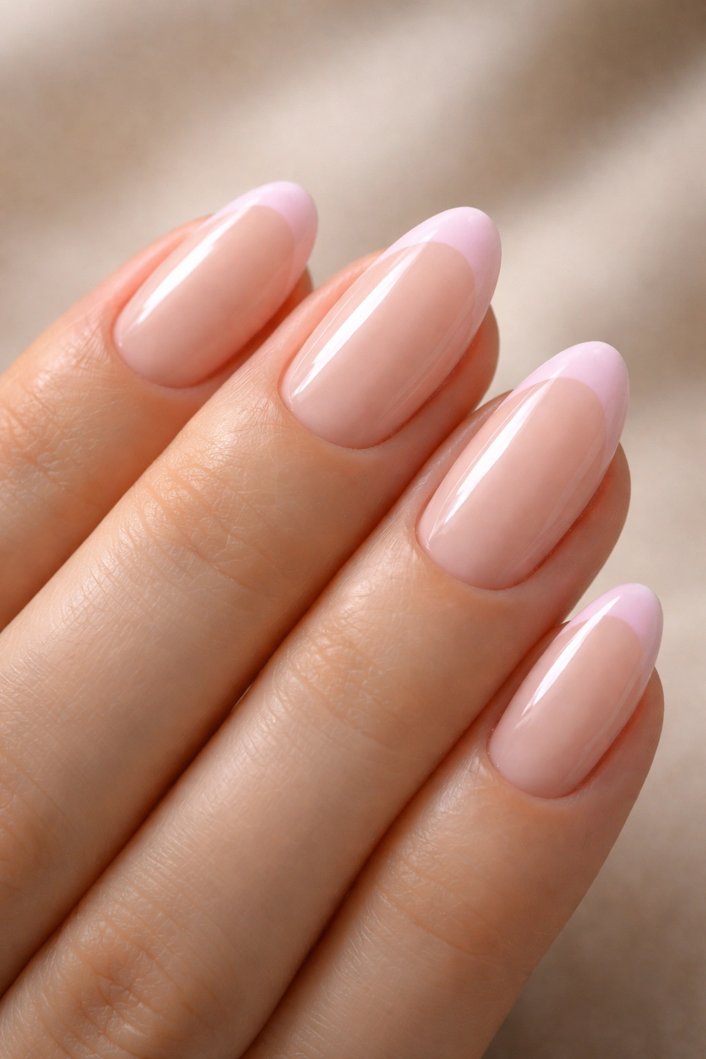Close-up of an extra-short almond nail with a baby pink French tip on pale nude base.