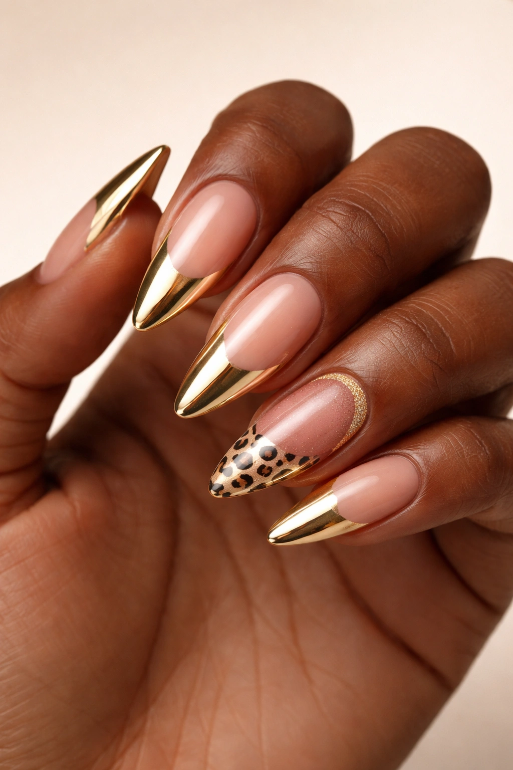 Close-up of dark-skinned hand with acrylic nails featuring gold chrome tips, leopard print accent, and ombre designs