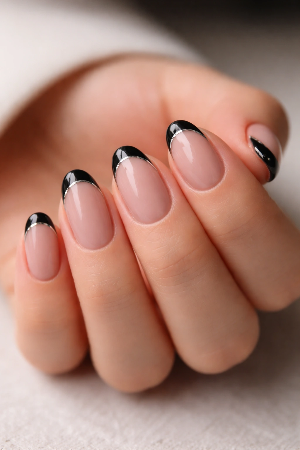 Close-up of short oval nails with black tips and slim chrome outlines