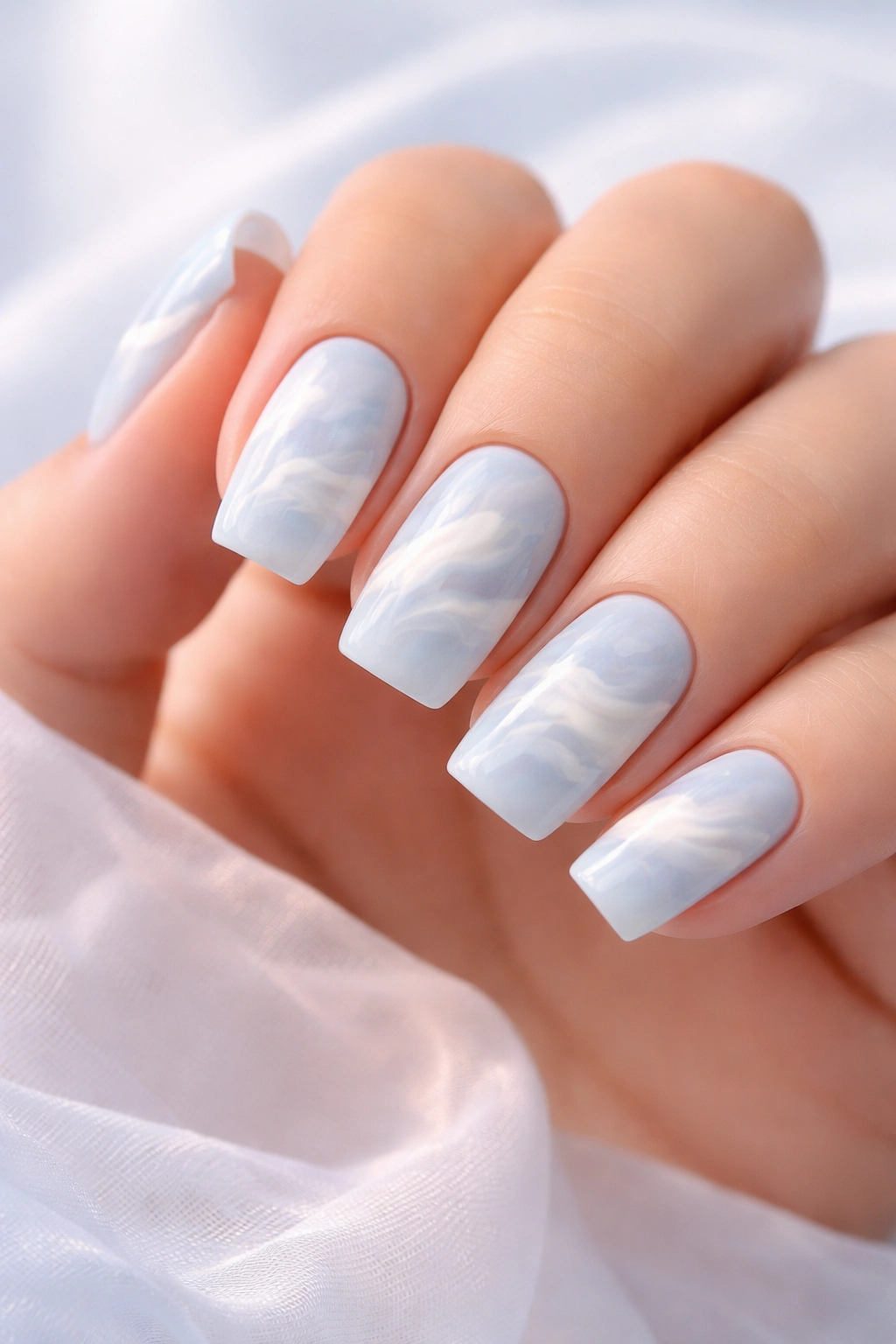 Close-up of soft square nails with cloud-like pastel swirls on pale blue base