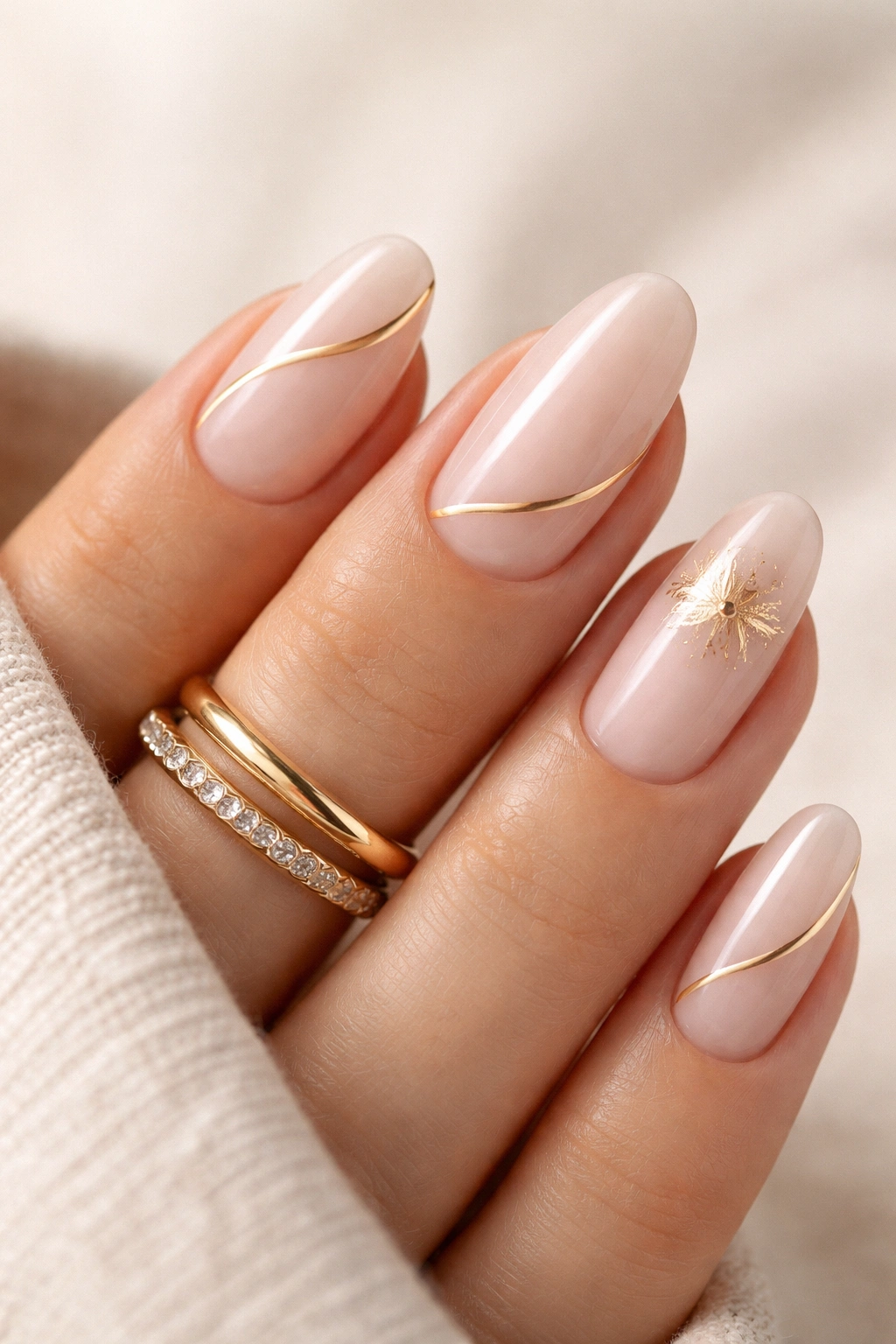 Hand with minimalist gold-line and gold-foil nail art with a gold ring