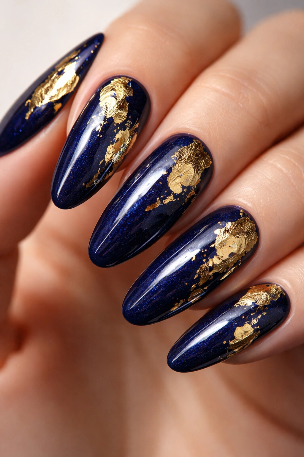 Long oval nails with deep navy base and irregular gold foil shapes
