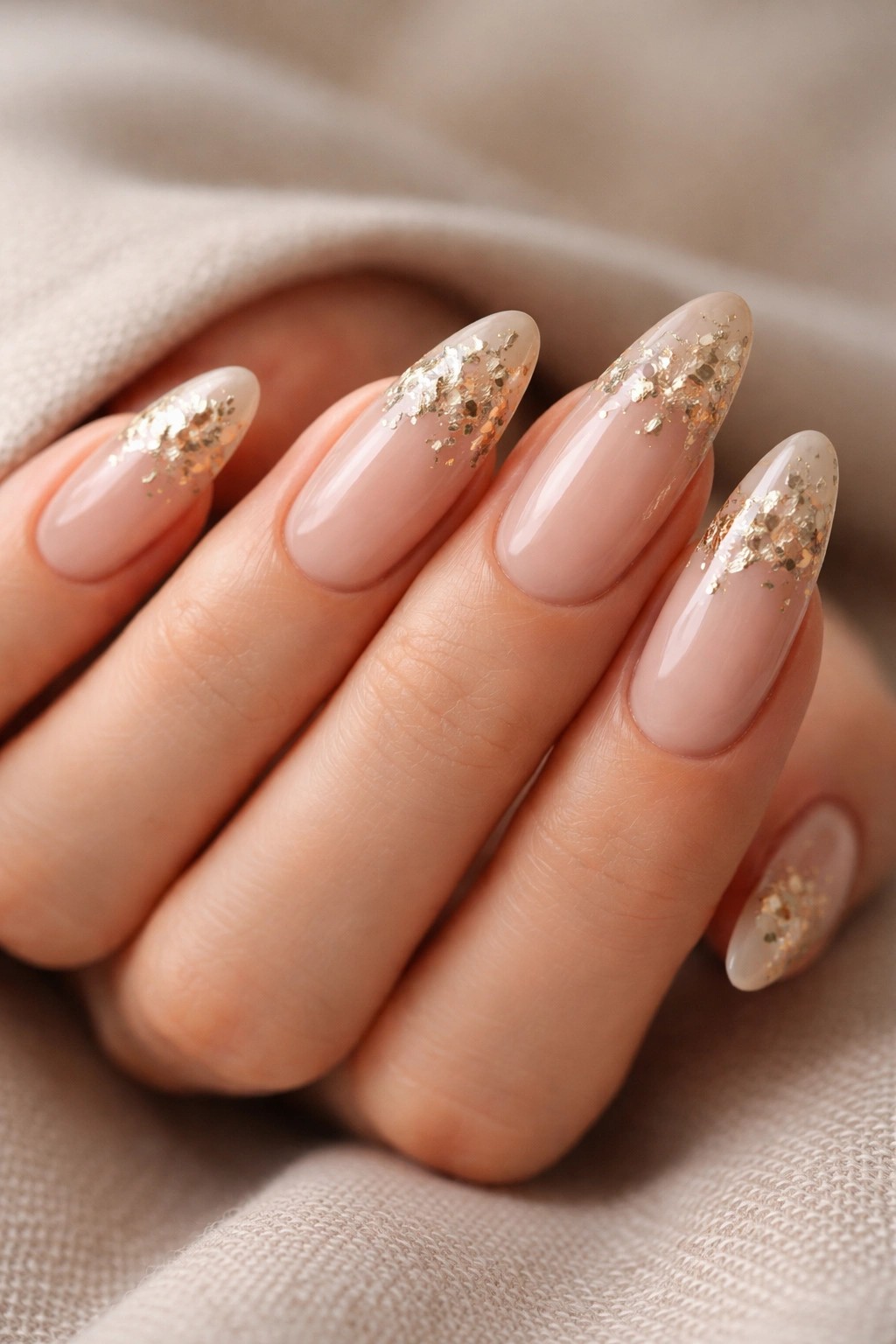 Close-up of extra-long oval nails with gold foil clusters on a nude base