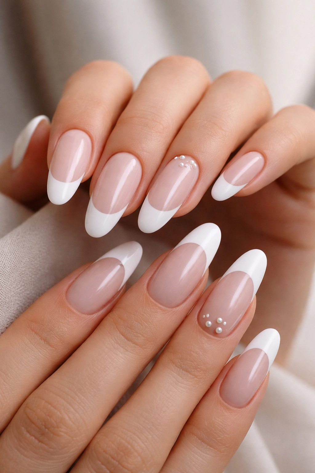 Close-up of long oval nails with classic white French tips and tiny pearl accents near the cuticles