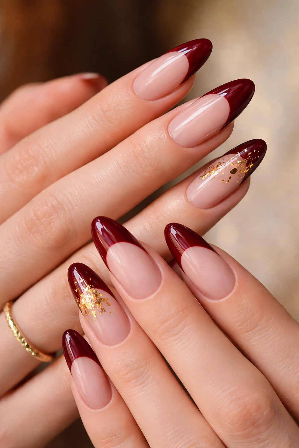 Close-up of long oval nails with deep red French tips and gold leaf detail