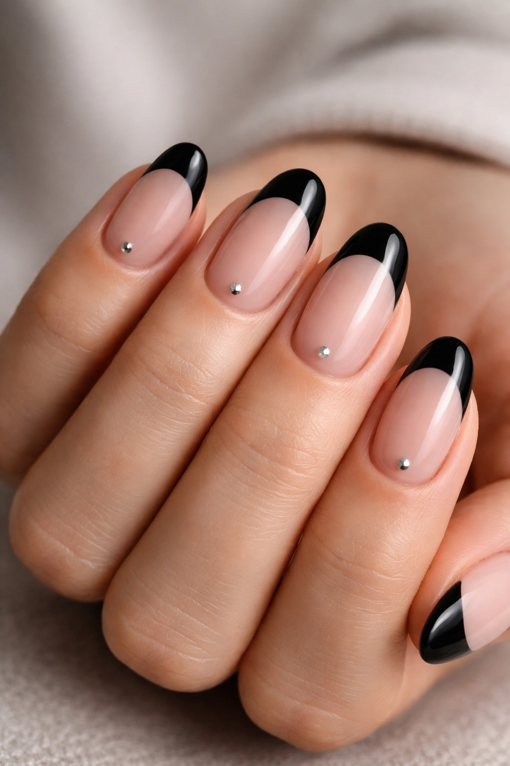 Close-up of short oval nails with black tips and tiny studs near the cuticle