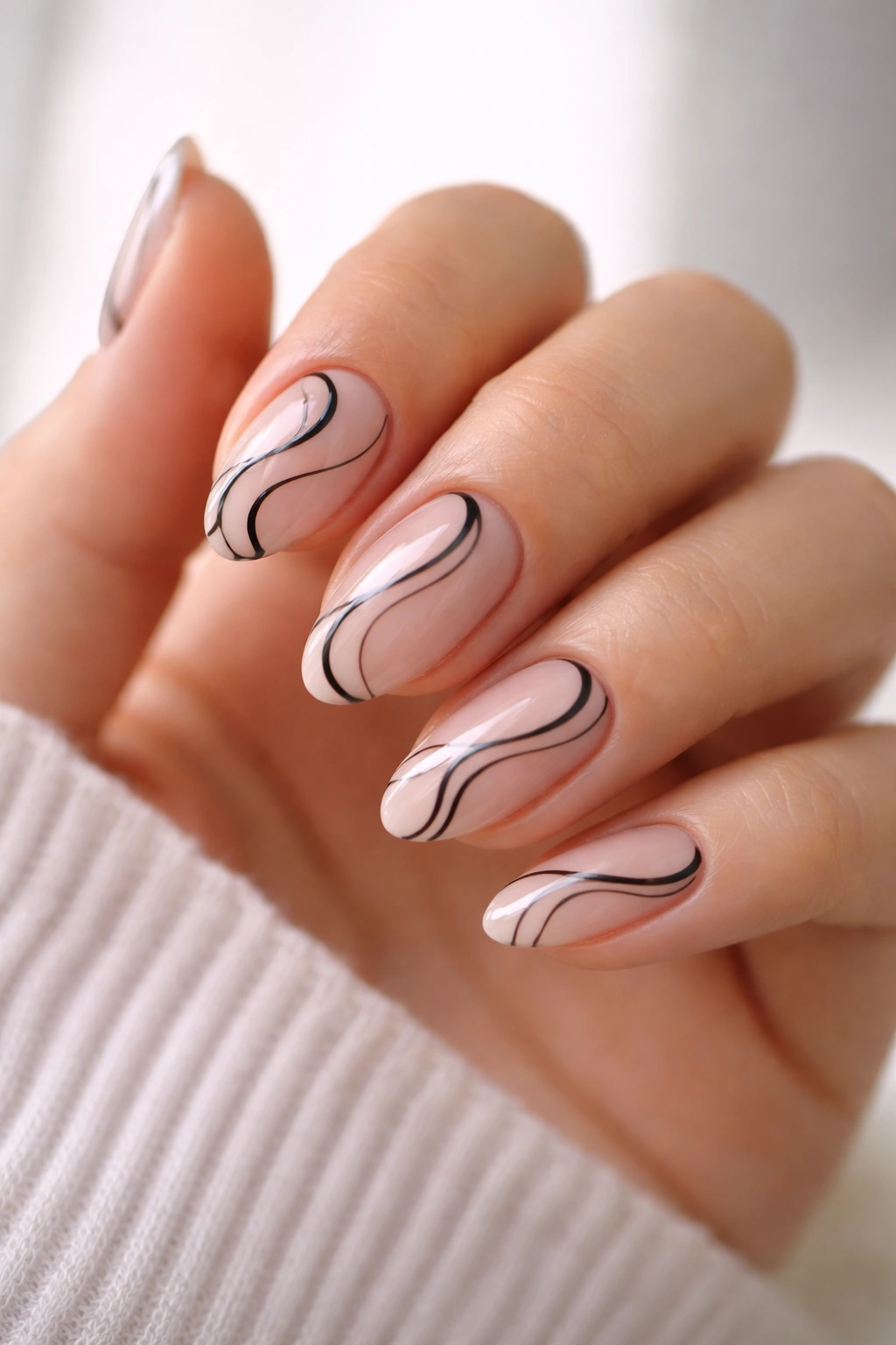 Close-up of short almond nails with sheer base and black swirl patterns