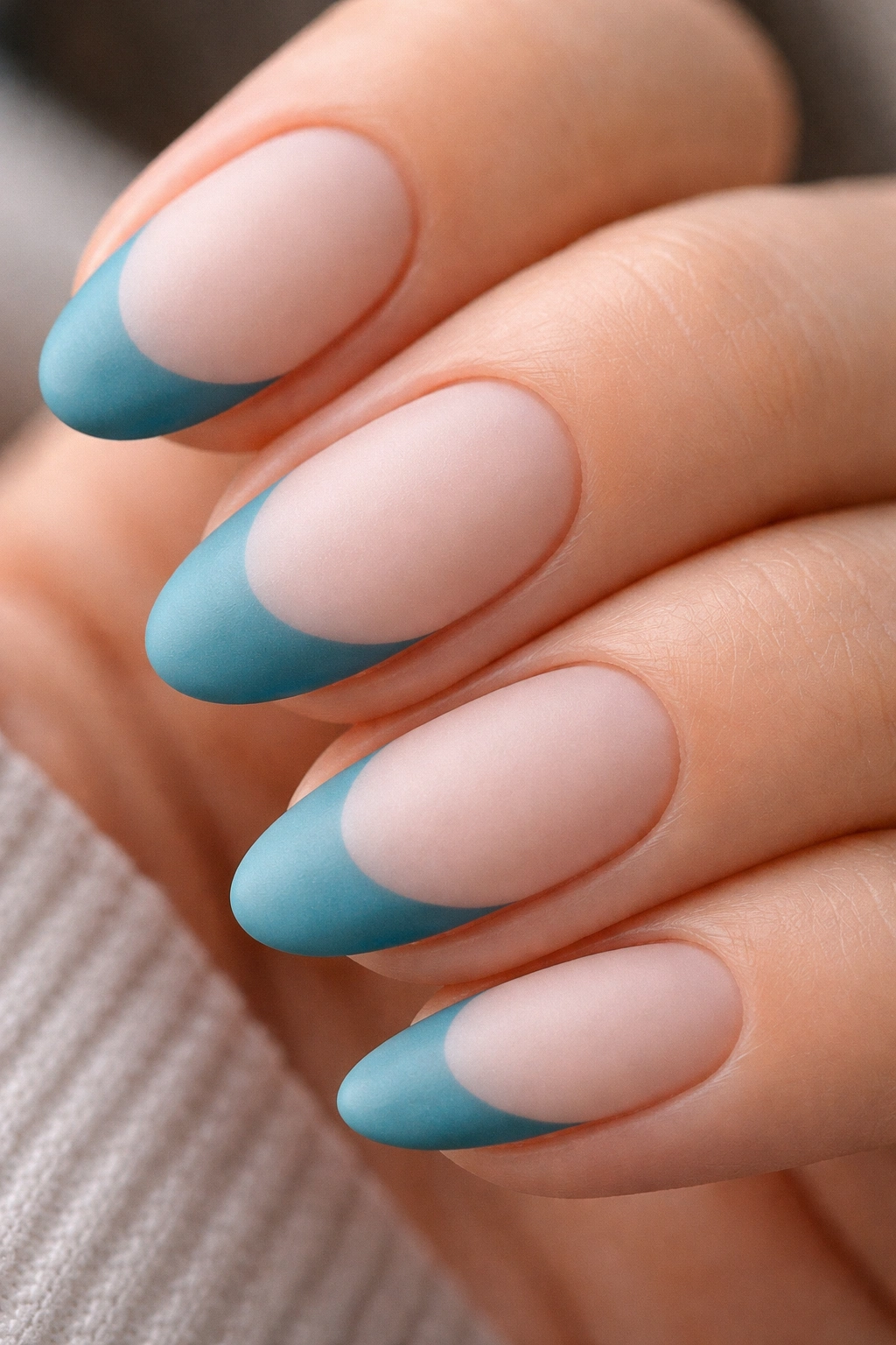 Close-up of almond nail with teal blue matte French tip.