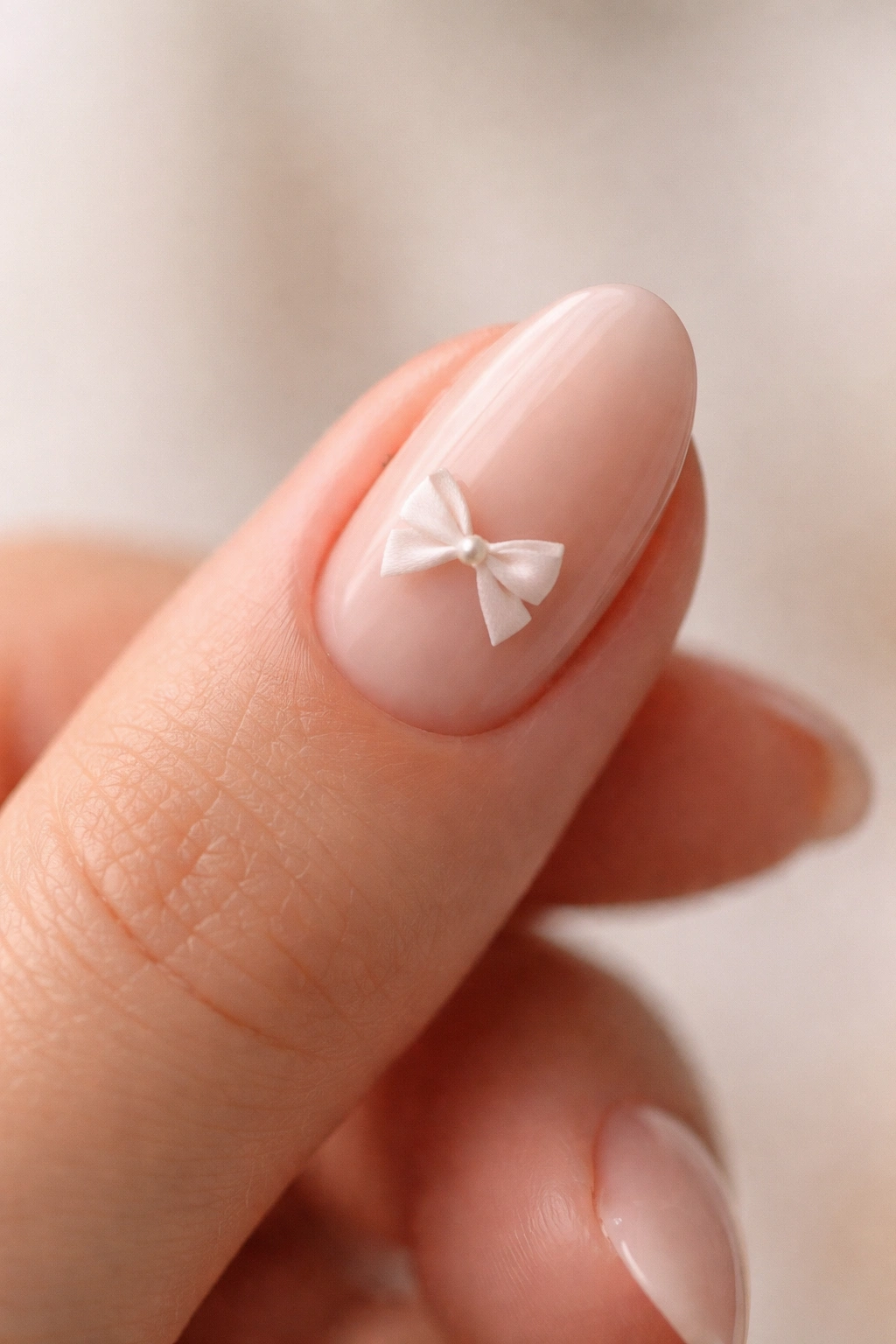 Close-up of a tiny white bow accent on a short almond nail with nude base.