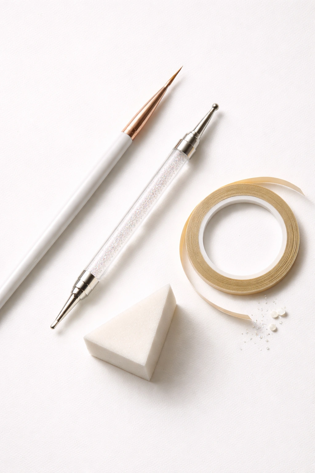 Flat lay of manicure tools including liner brush, dotting tool, sponge, and tape.
