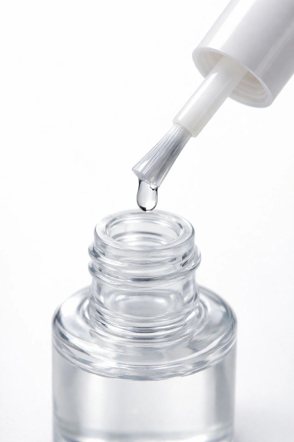 Close-up of a clear nail glue bottle with a precision brush and adhesive bead