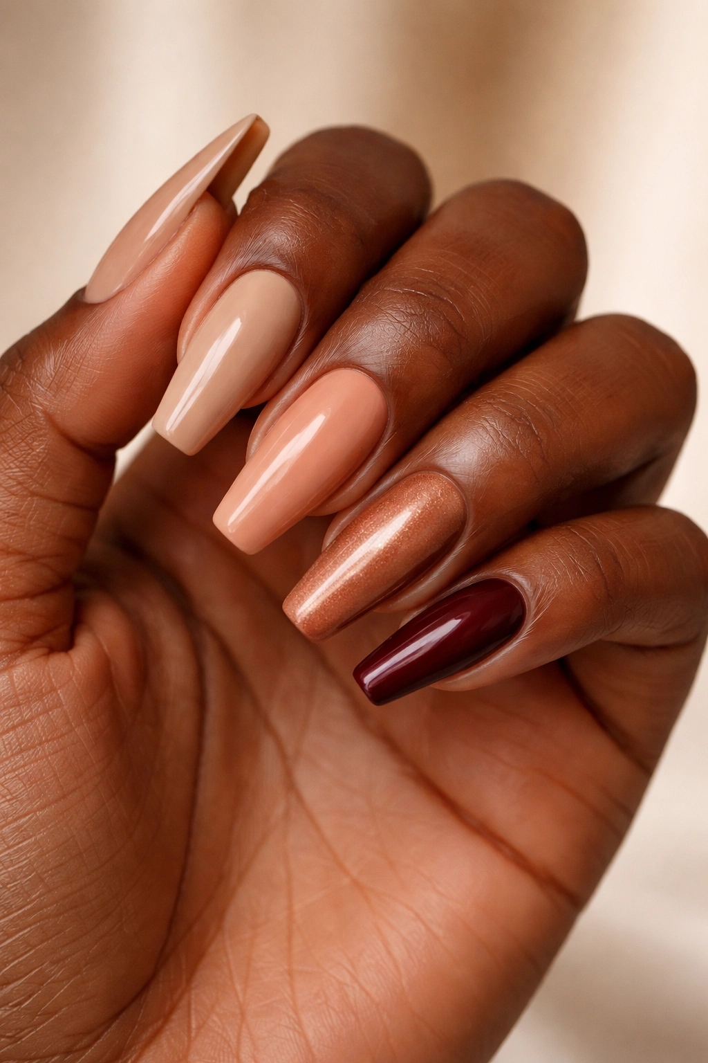 Close-up of dark-skinned hand with nails in neutral to burgundy shades to illustrate shade choices