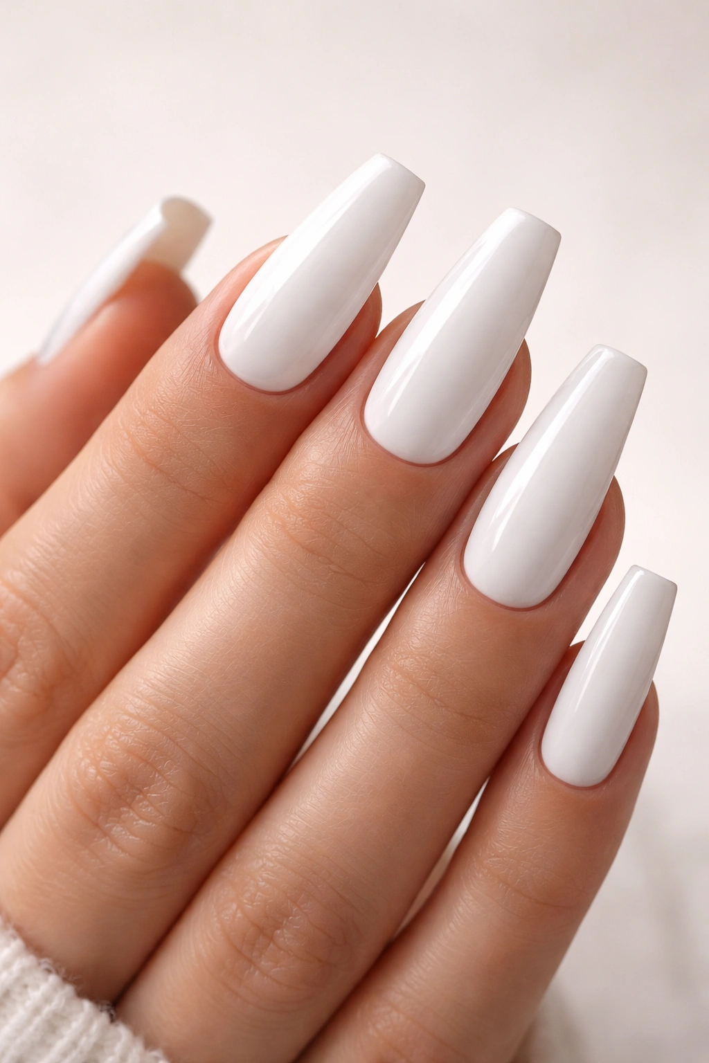 Close-up of coffin-shaped white acrylic nails on a hand.