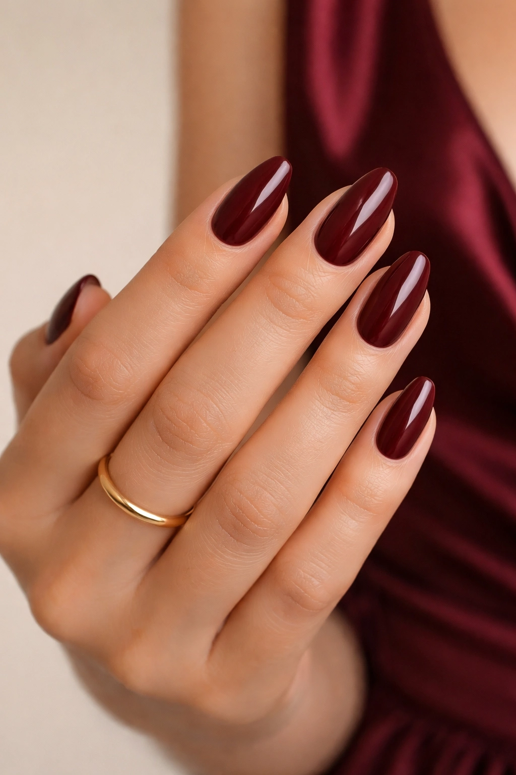 Nails with burgundy polish accented by a gold ring