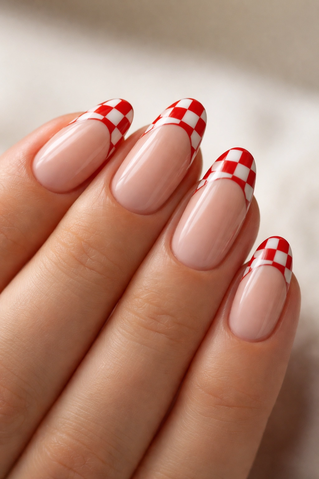 Close-up of short almond nails with red checkerboard French tips along the curved edge