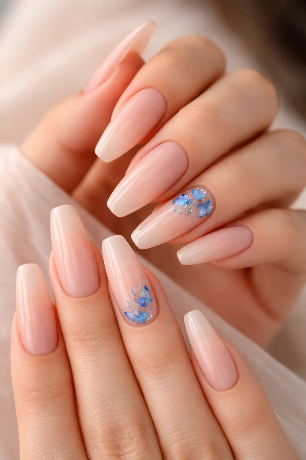 Close-up of sheer nude nails with blue butterfly clusters on accent nails