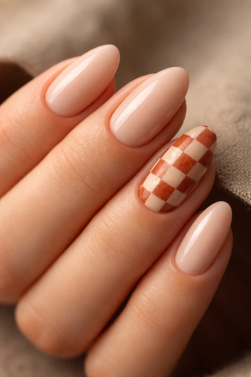 Close-up of rust and nude checkerboard short almond nails with two accent nails