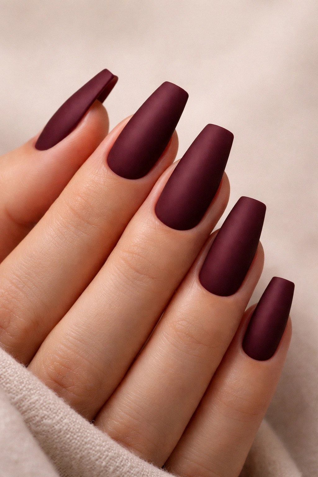Close-up of coffin nails in deep burgundy matte finish on a neutral background
