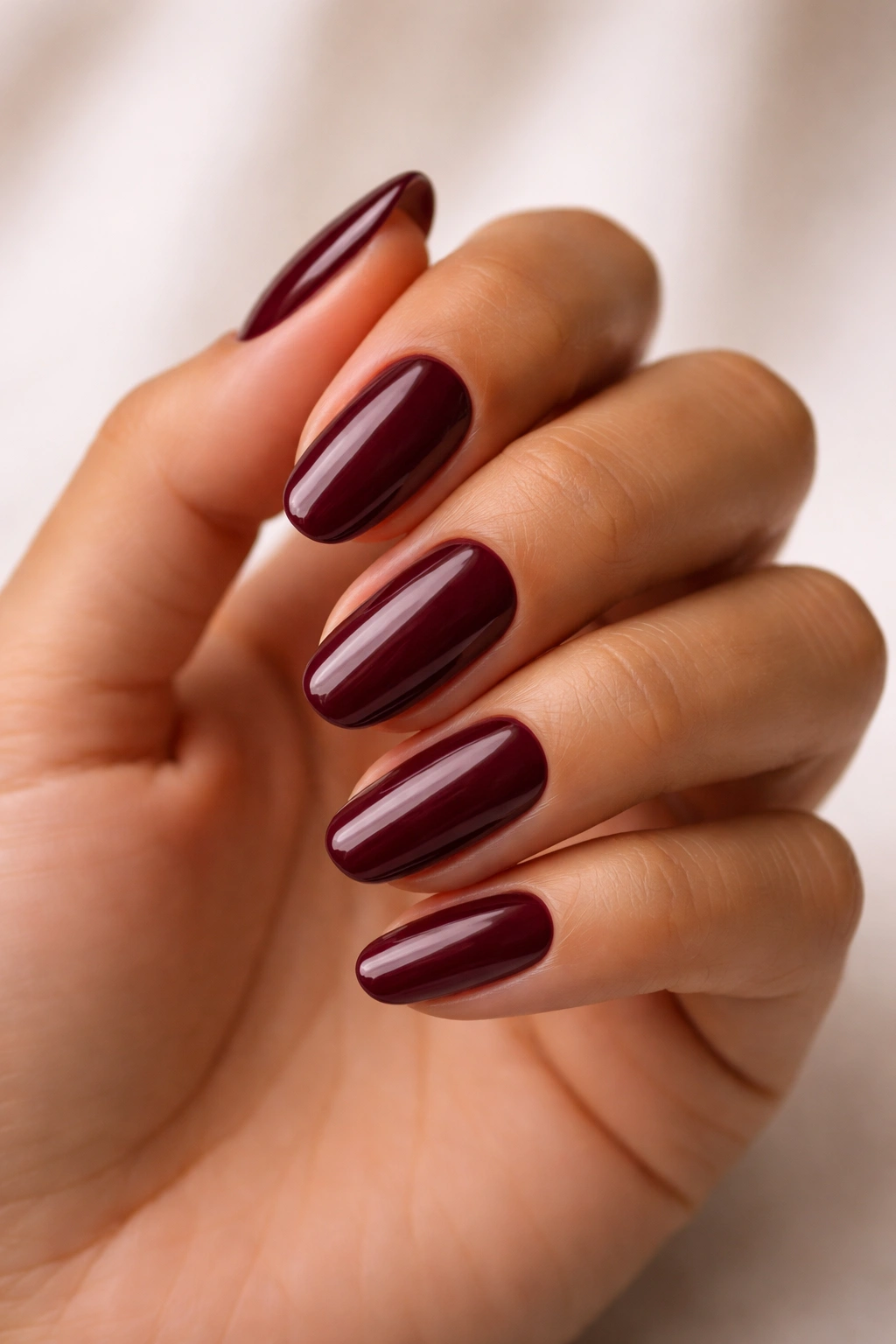 Hand with burgundy nails on medium skin tone against neutral background