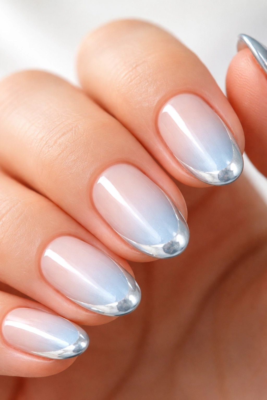 Close-up of a short almond nail with a light blue chrome edge and pearly finish