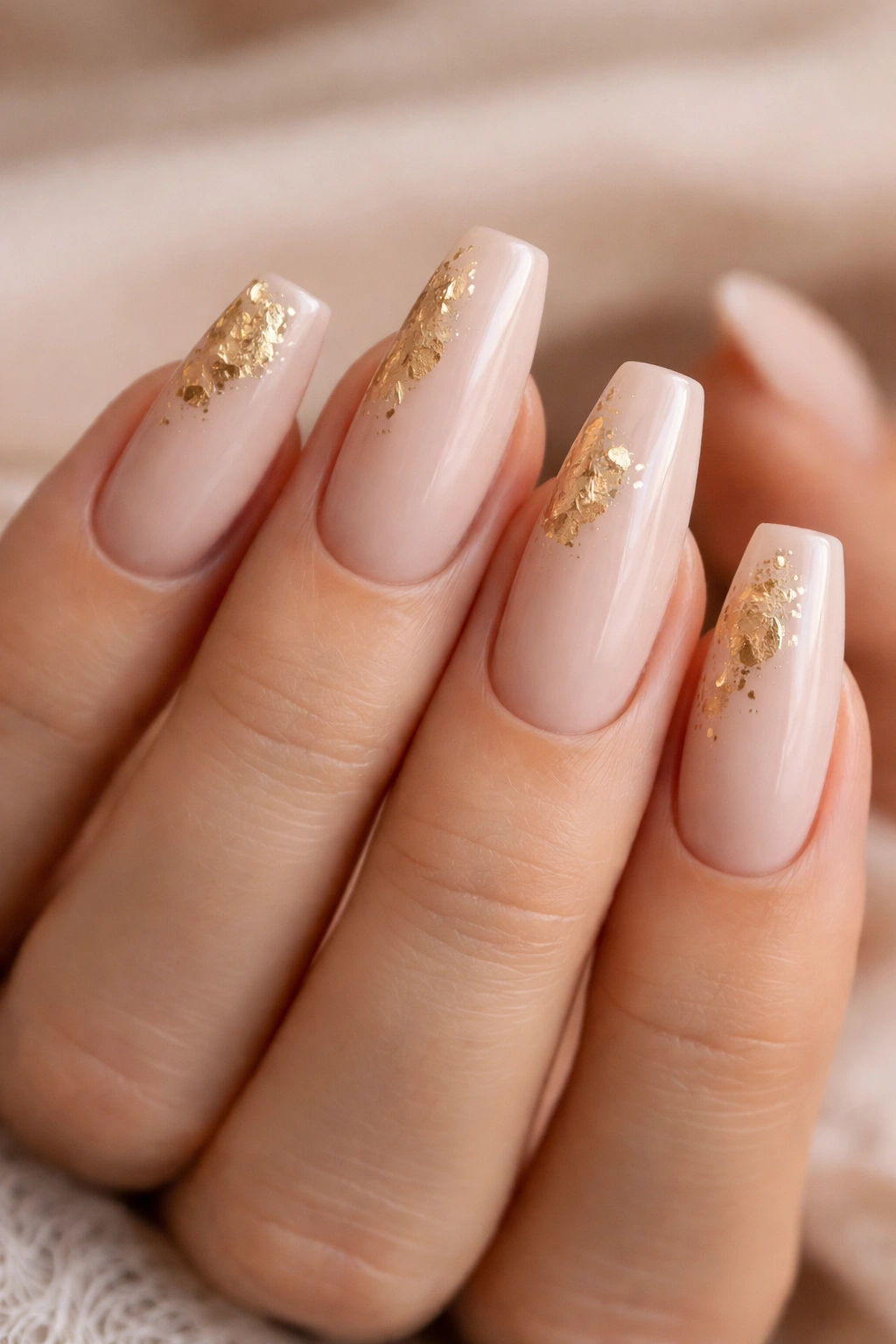 Close-up of coffin nails in soft nude with gold leaf accents on a neutral background