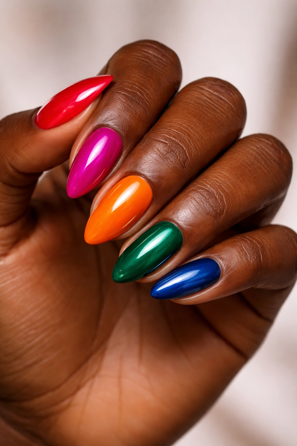Nails painted vivid red, magenta, orange, emerald, sapphire on deep skin.