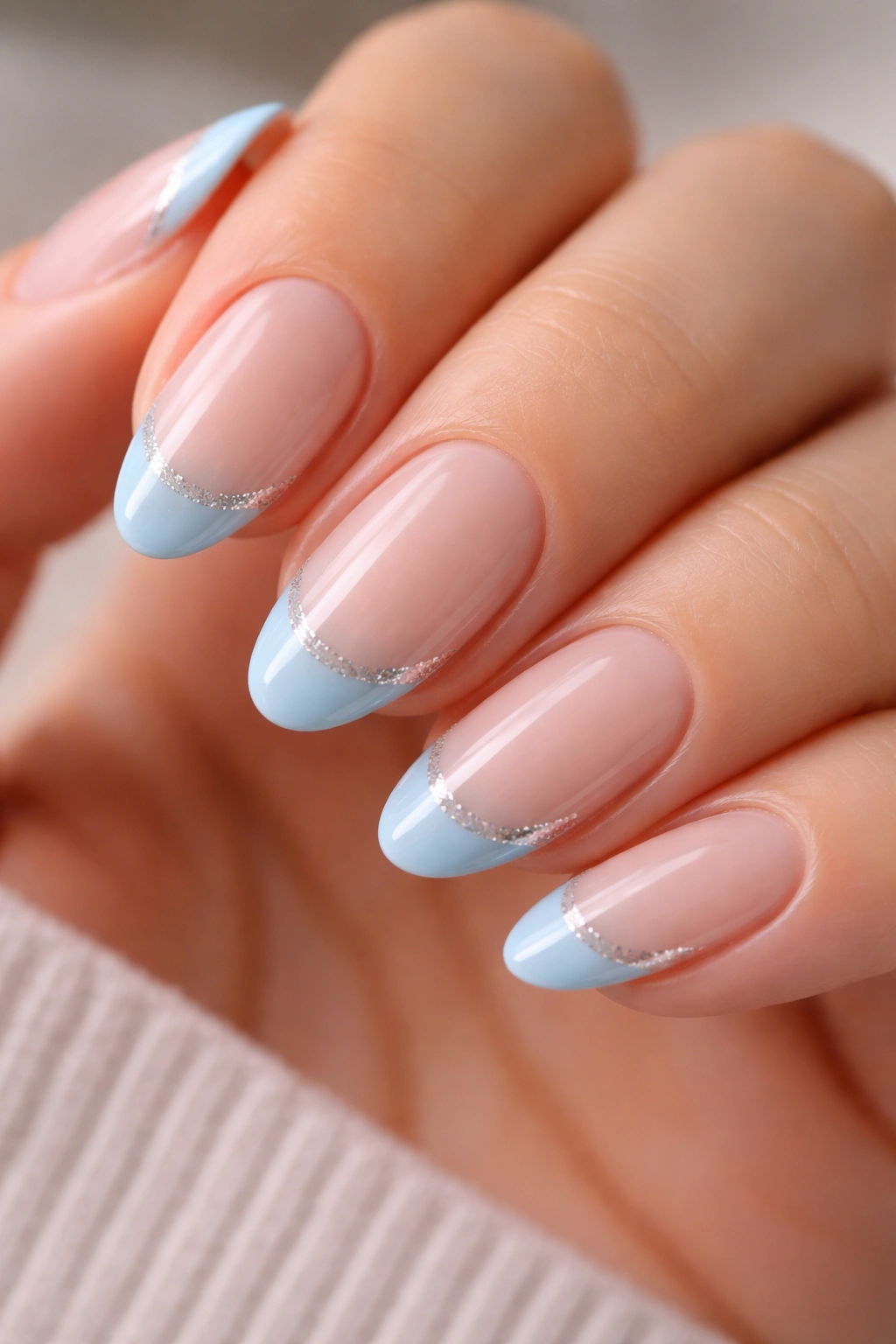 Close-up of blue French tips outlined with fine glitter on short almond nails