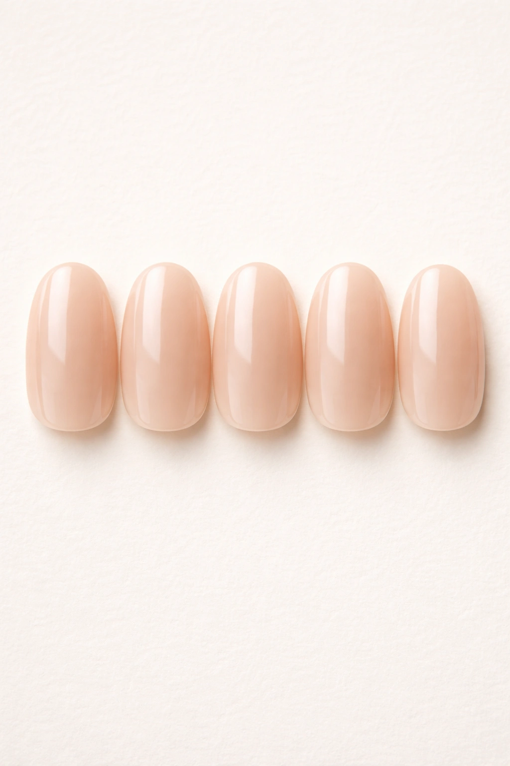 Close-up of five sheer nude short oval press-on nails on a neutral background