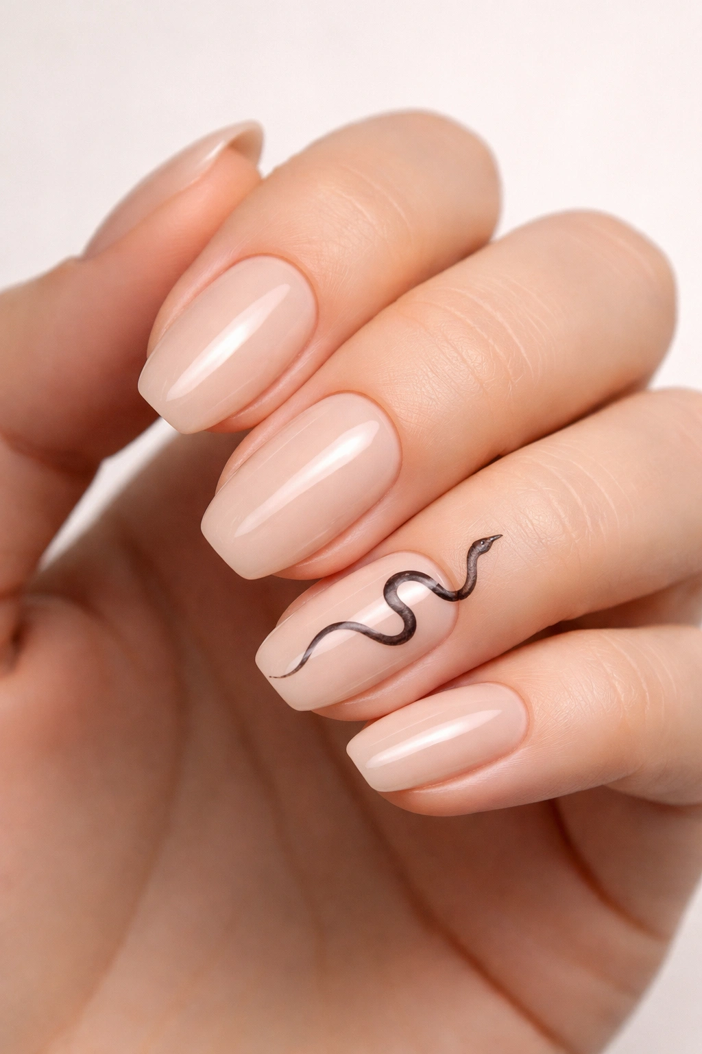 Close-up of nude nails with a single minimalist black snake accent on the ring finger