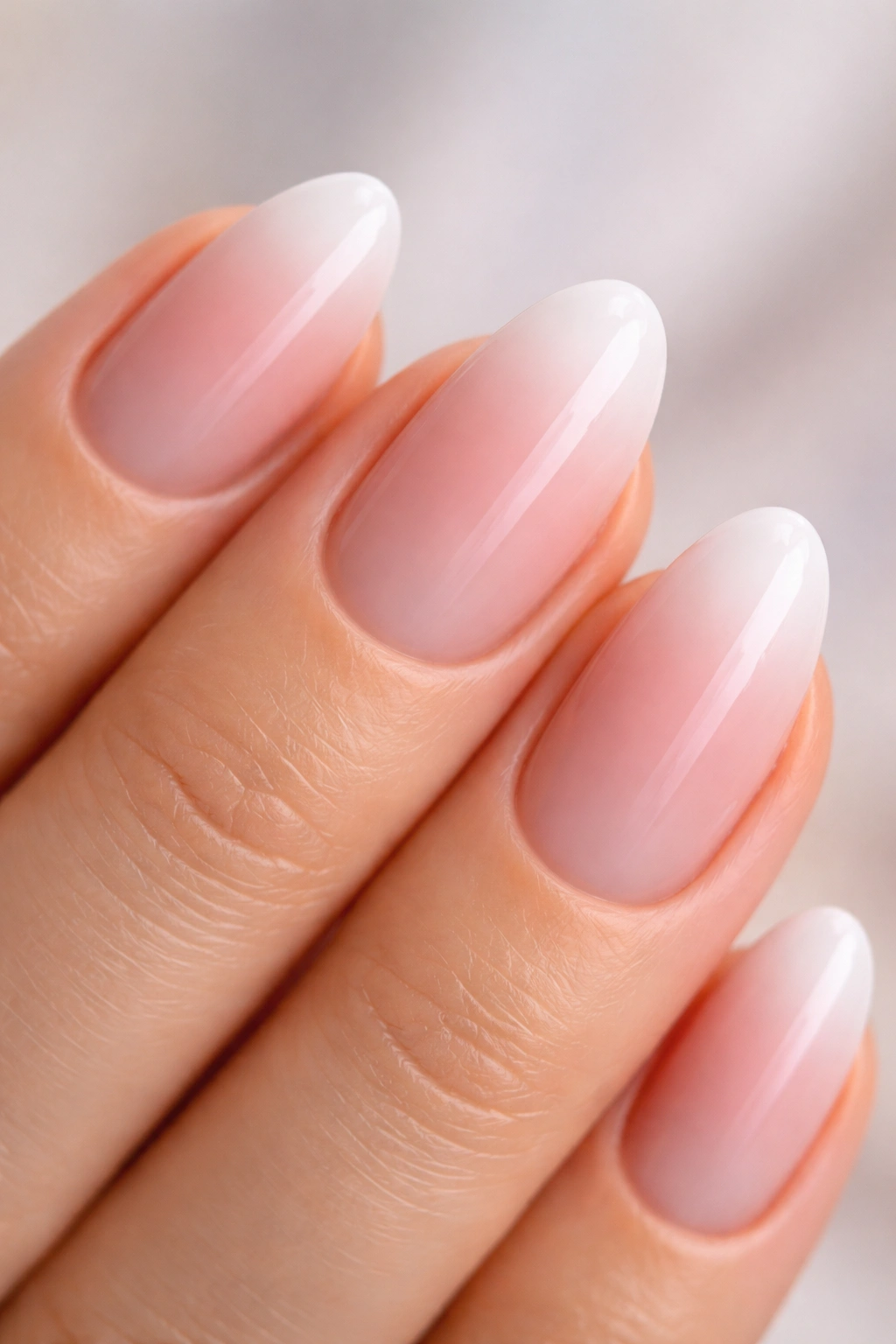 Close-up of a short almond nail with pink-to-white ombre on a neutral background