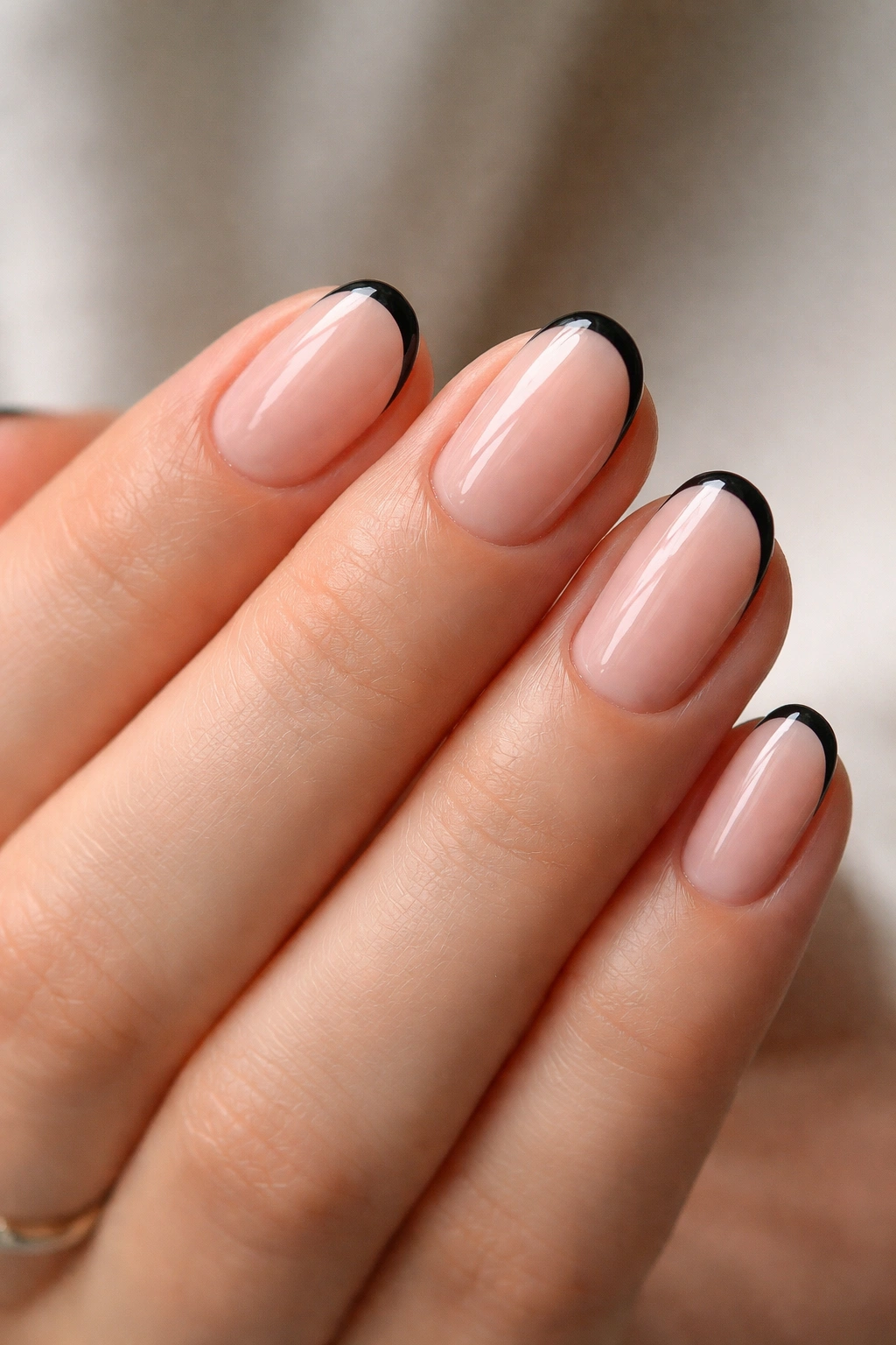 Close-up of short oval nails with a thin black French tip on a sheer pink base