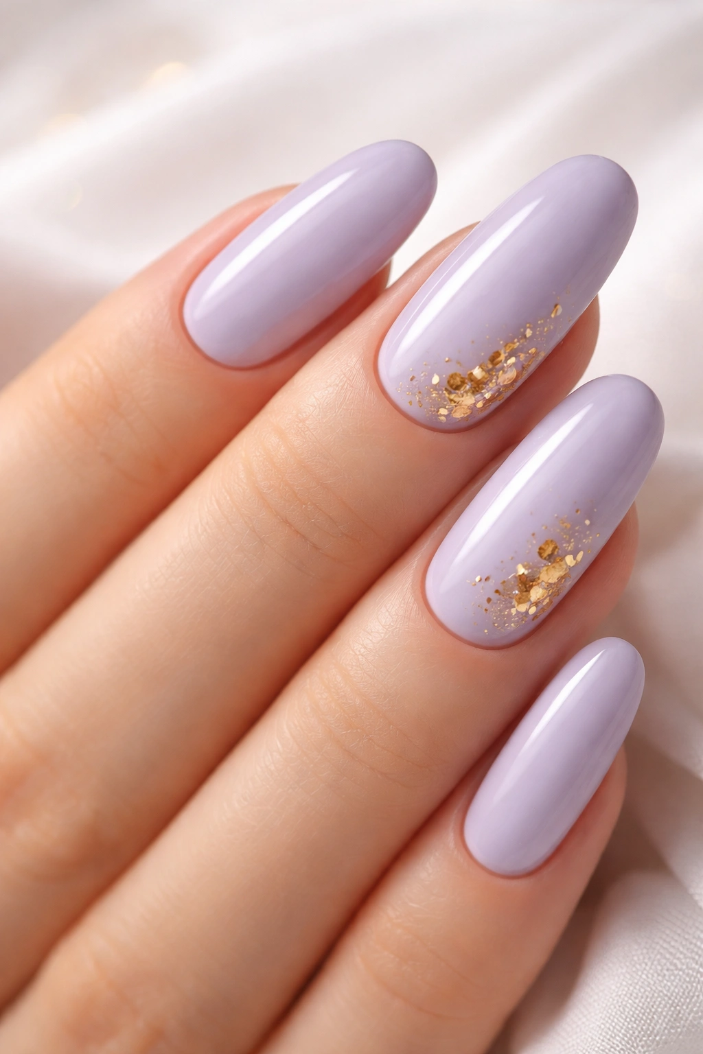 Close-up of long round nails in pale lavender with gold leaf accents.