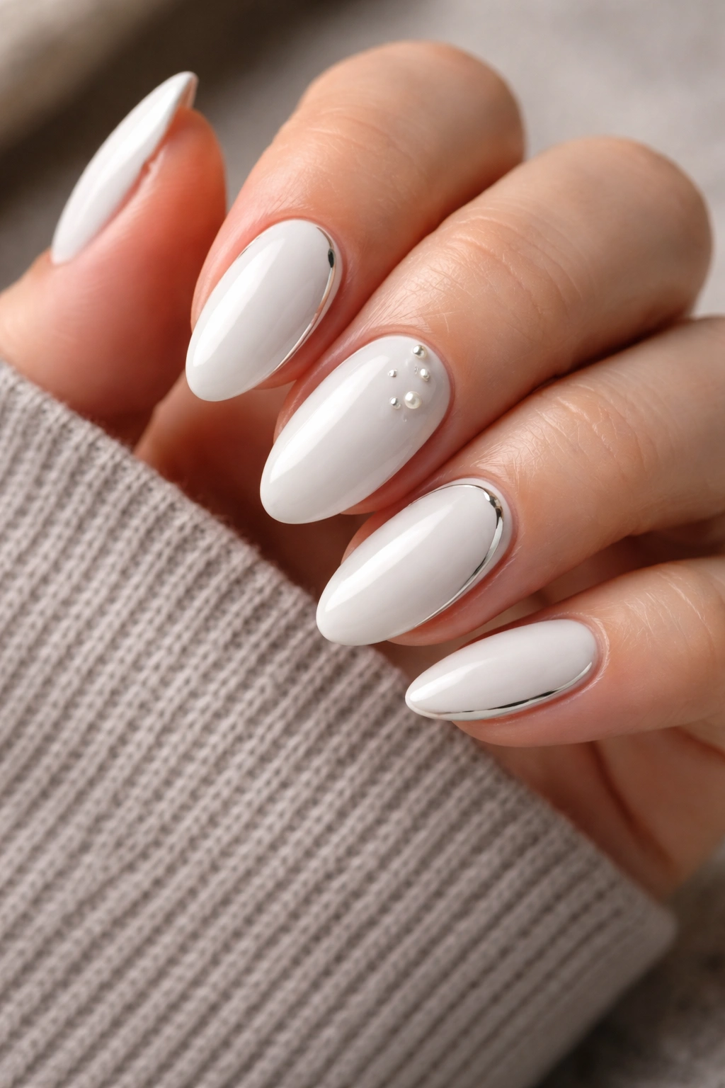 Close up of white almond nails with tiny pearl and chrome accents on a hand