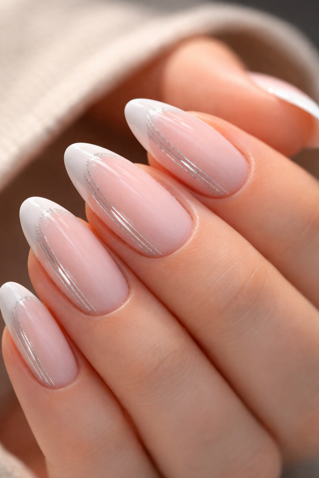 Close-up of a short almond nail with soft pink base, white tip and silver striping