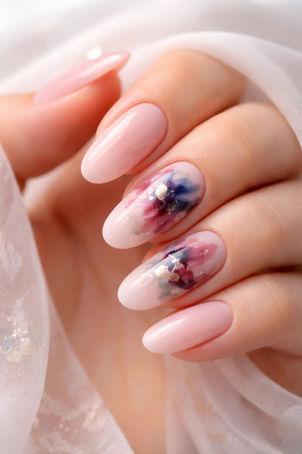 Close-up of long round nails with soft pink base and abstract watercolor splashes.