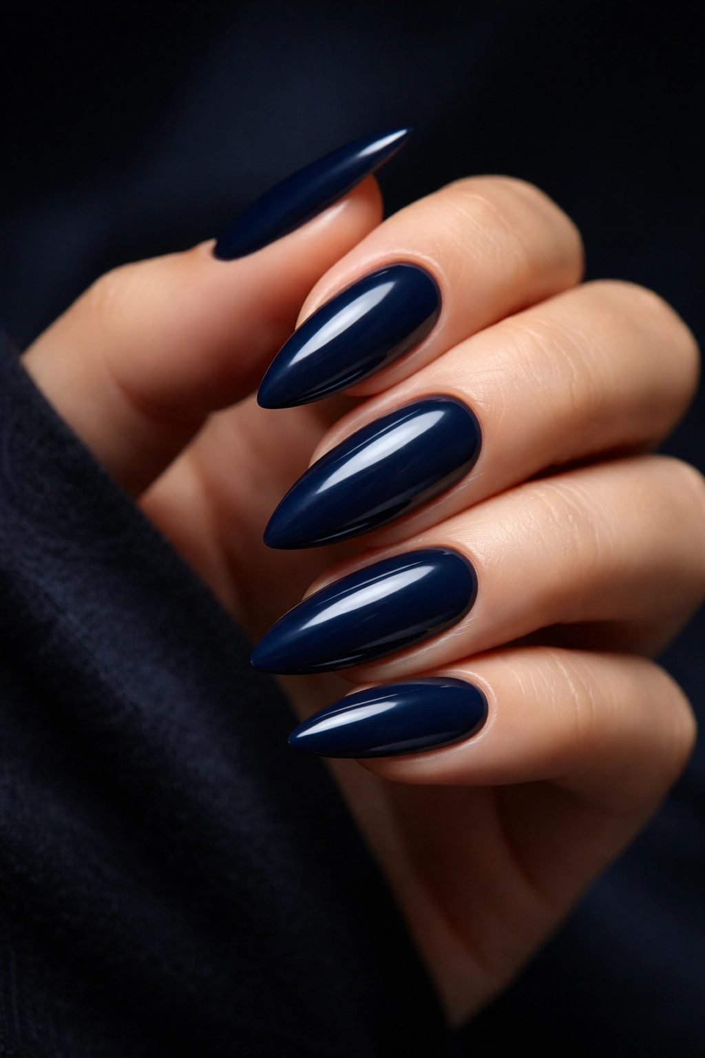 Close-up of deep navy almond nails with moody studio lighting