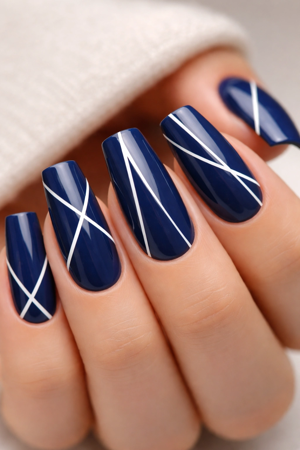 Close-up of medium coffin nails painted navy blue with white geometric patterns on a soft neutral backdrop