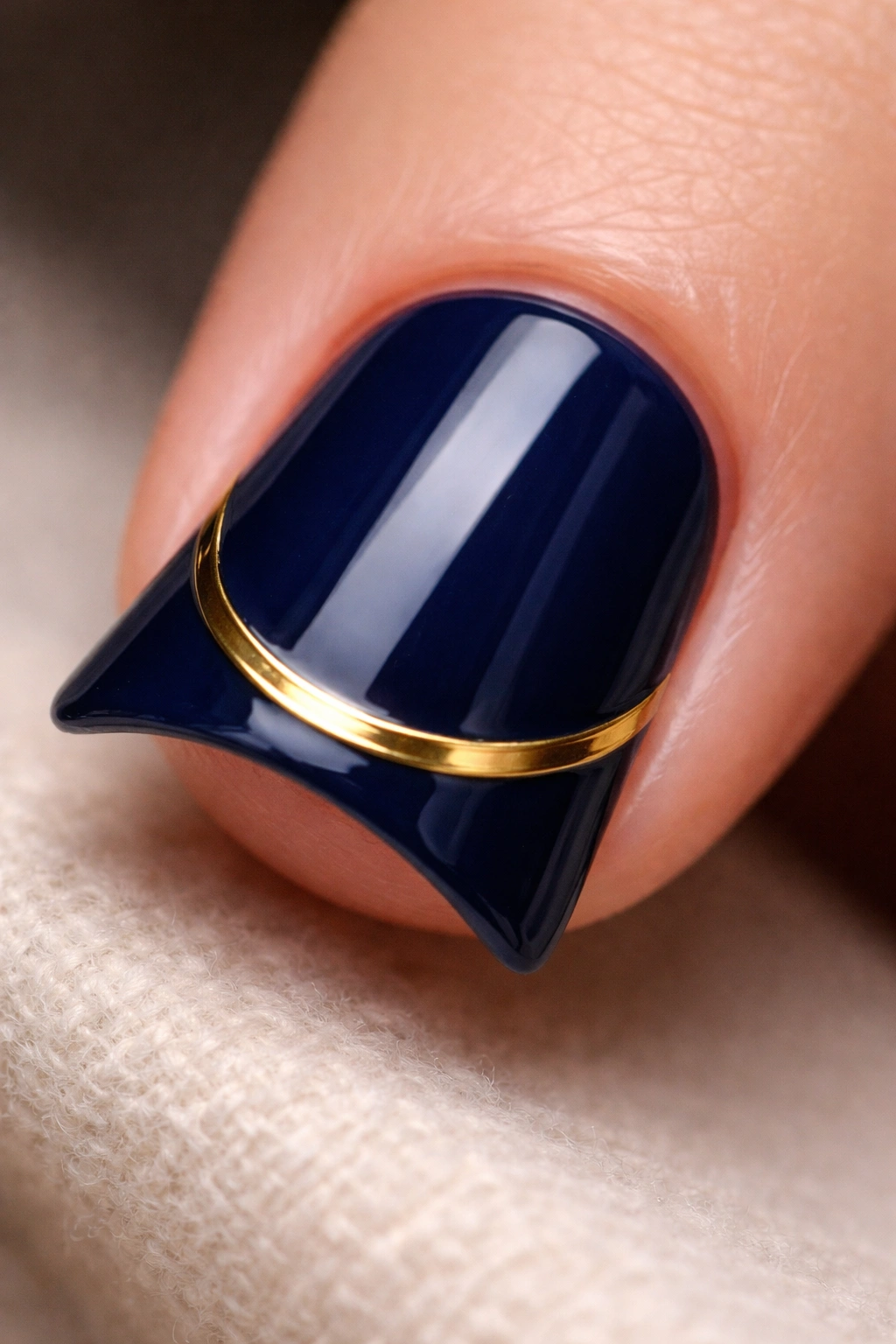 Close-up of a short nail with navy blue base and a curved metallic gold accent line along the duck tip