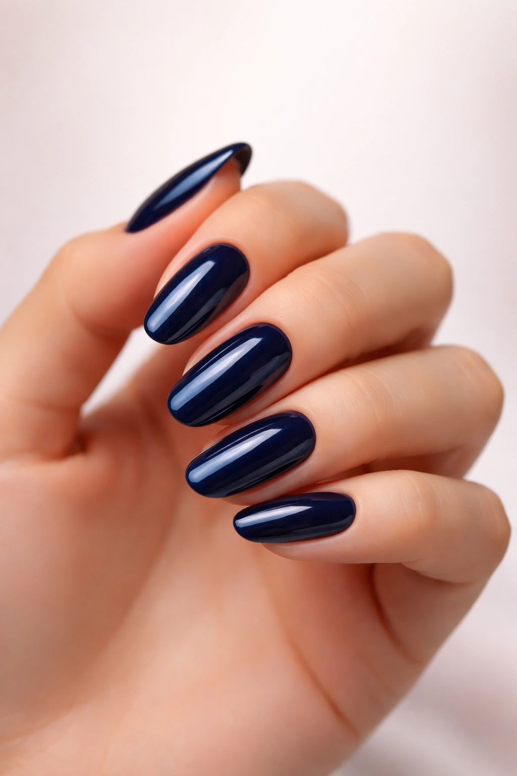 Close-up of glossy navy blue nails on a hand with a neutral background