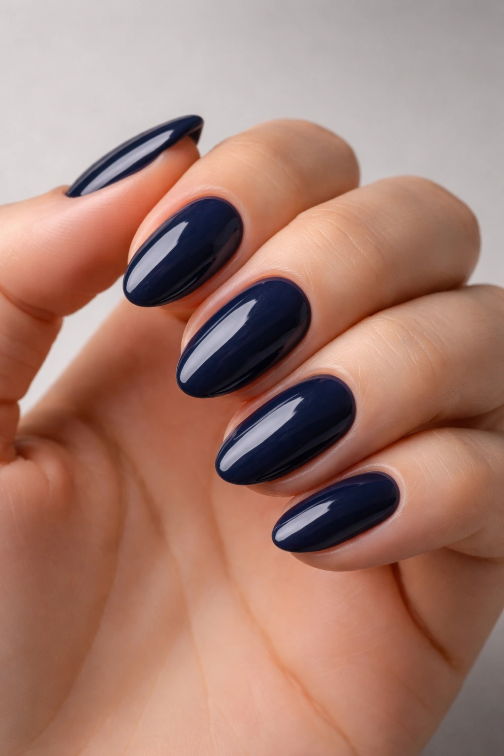 Close-up of short almond nails painted navy blue with a high-gloss finish and clean sidewalls