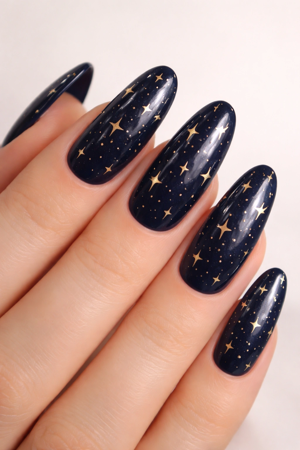 Navy blue oval nails with tiny gold stars scattered.