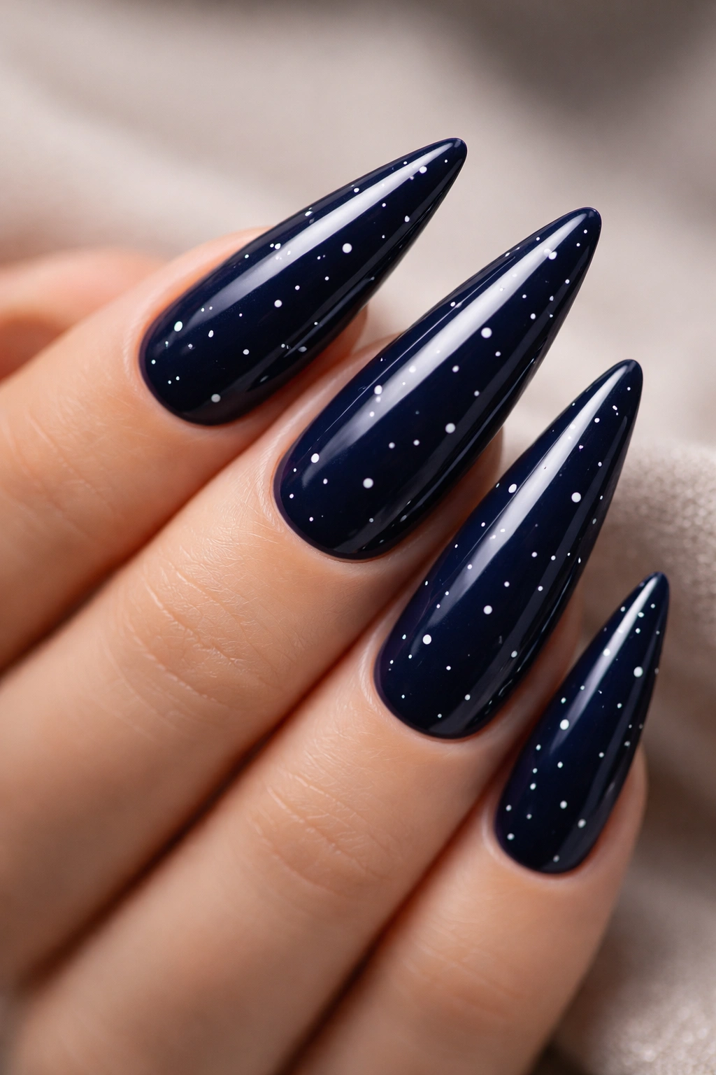 Close-up of navy blue stiletto nails with small white dots in a minimalist pattern