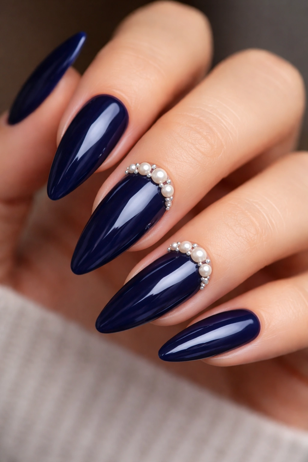Close-up of navy blue nails with pearl embellishments on a neutral background