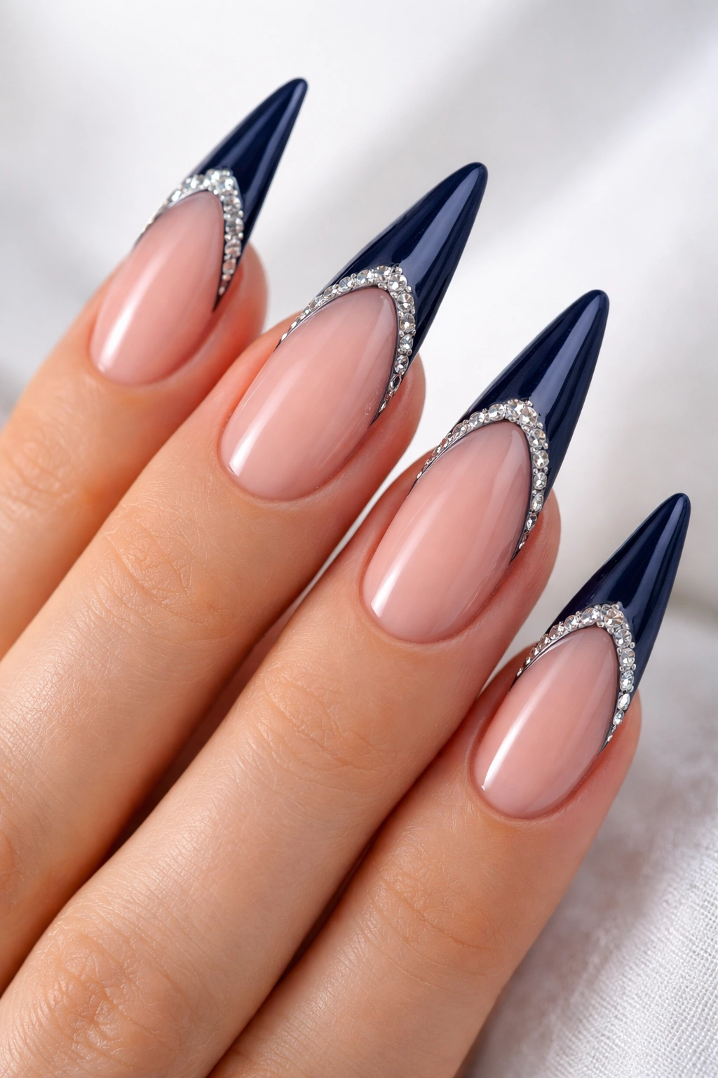 Close-up of navy blue French-tip stiletto nails with rhinestones along the tip transition