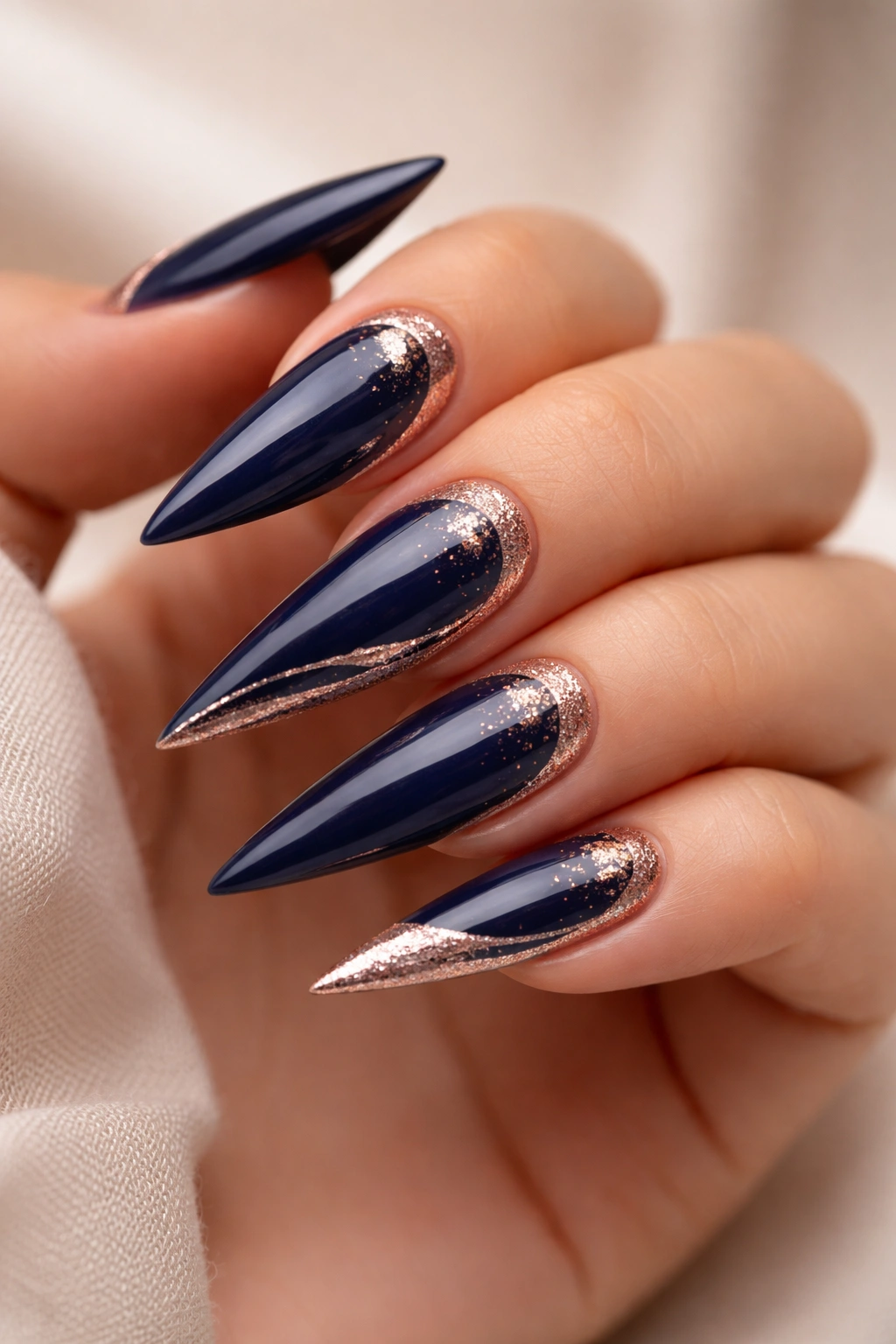 Close-up of navy blue stiletto nails with rose gold accents on a neutral background