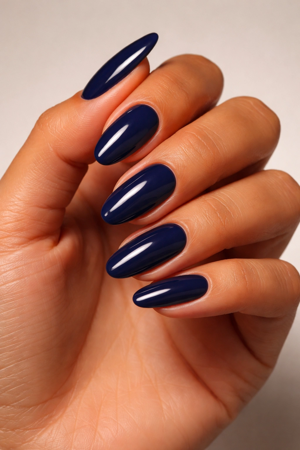 Close-up of a tanned hand with navy blue nail polish.